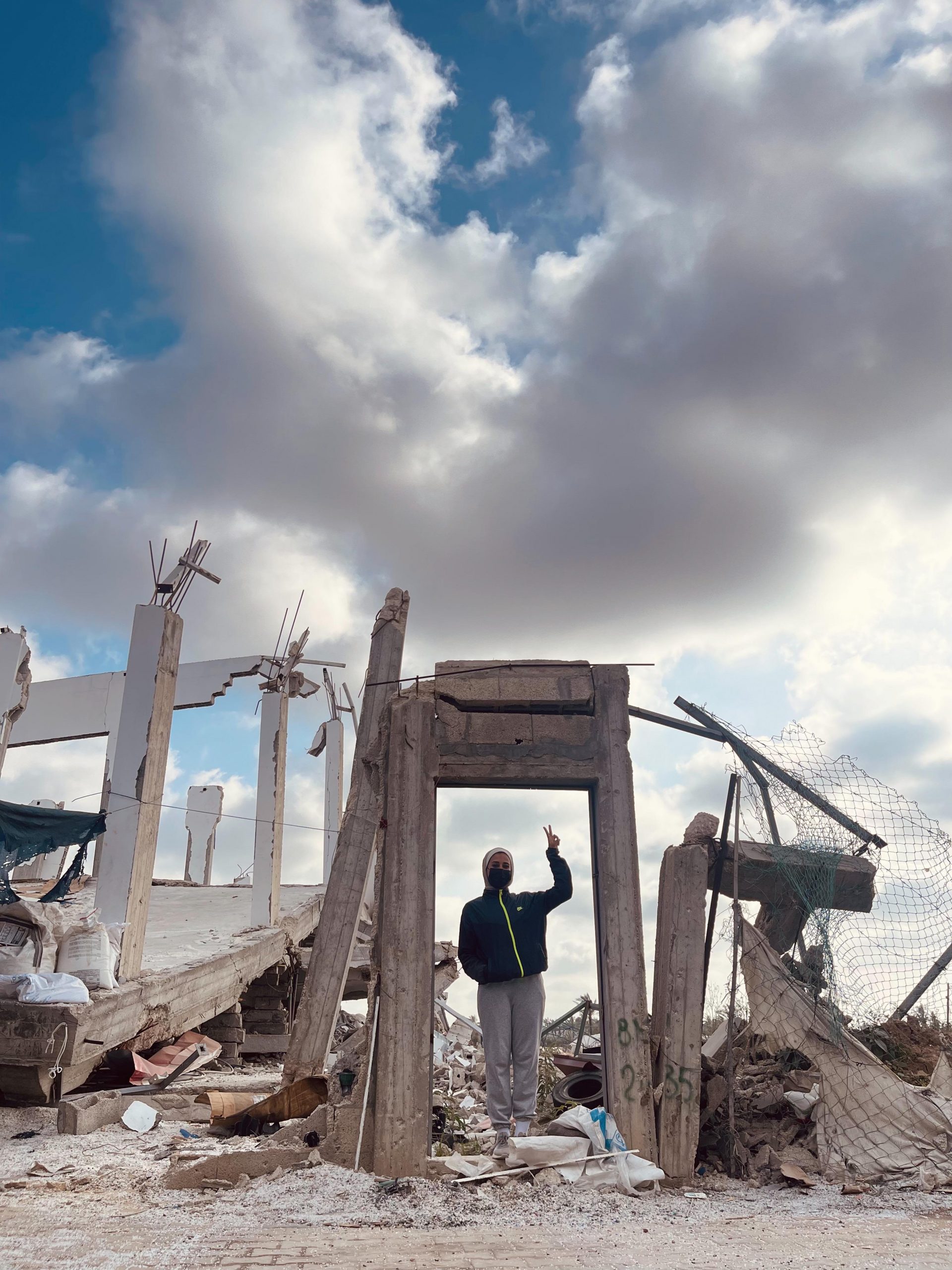 About Gaza 40 student standing in a doorway of a demolished house